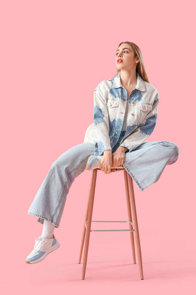 Young woman in light blue jeans sitting on pink background - Photo, Image