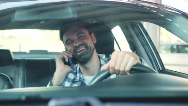 Sonriente tipo sentado en el coche mientras habla en el teléfono inteligente. Transporte, tecnología, estilo de vida. Movimiento lento - Metraje, vídeo