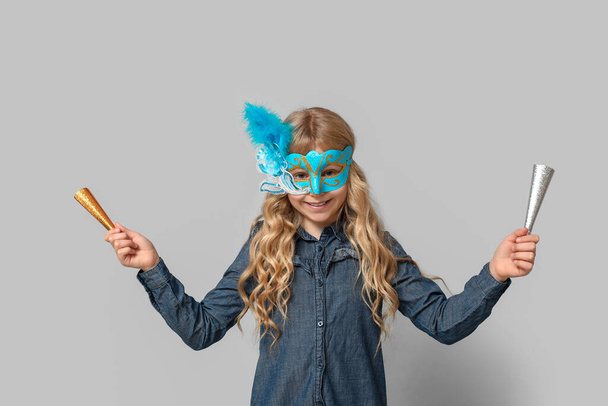 Χαριτωμένο κοριτσάκι με noisemakers φορώντας μάσκα καρναβάλι στο φως φόντο - Φωτογραφία, εικόνα