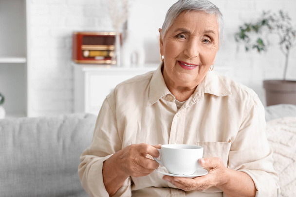 Vanhempi nainen, jolla on teetä sohvalla kotona - Valokuva, kuva