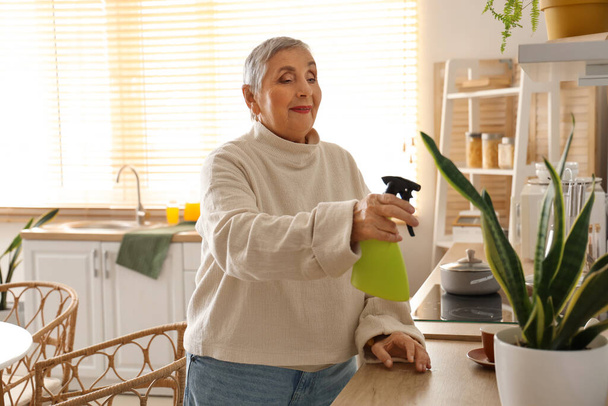 Oudere vrouw water geven plant in de keuken - Foto, afbeelding
