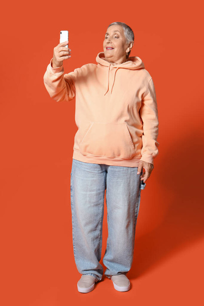 Seniorin mit Handy auf orangefarbenem Hintergrund - Foto, Bild
