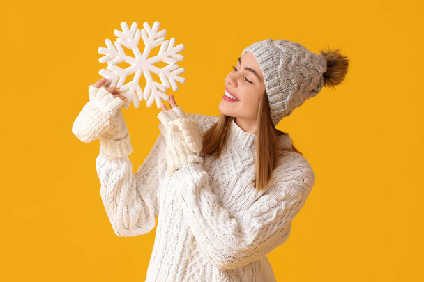 Sarı arka planda kar taneleri olan kışlık elbiseli mutlu genç kadın. - Fotoğraf, Görsel