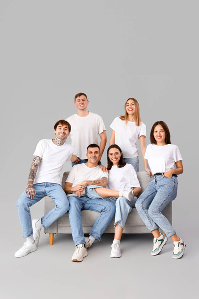 Група молодих людей у стильних джинсах, що сидять на дивані на світлому фоні - Фото, зображення