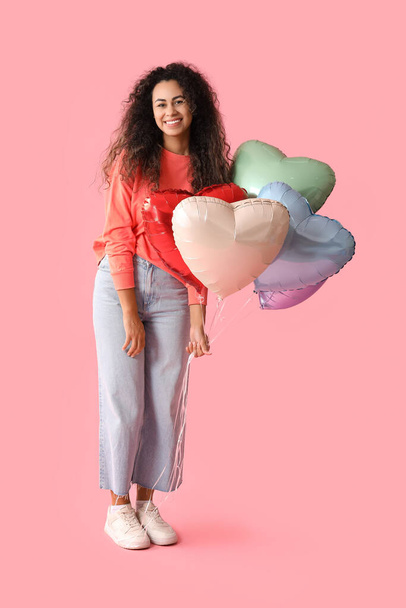 Kaunis nuori afroamerikkalainen nainen, jolla on sydämen muotoiset ilmapallot vaaleanpunaisella taustalla - Valokuva, kuva