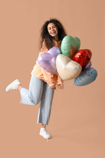 Beautiful young African-American woman with heart shaped air balloons on brown background - Photo, Image