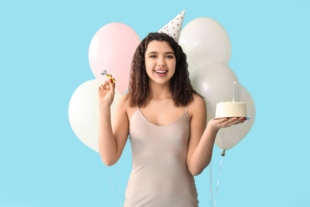 Schöne junge Frau in Partyhut mit süßem Kuchen und Luftballons feiert Geburtstag auf blauem Hintergrund - Foto, Bild
