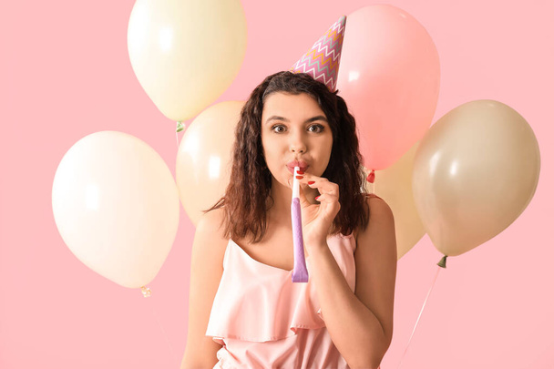 Hermosa joven con silbato de fiesta y globos aéreos celebrando el cumpleaños sobre fondo rosa - Foto, imagen
