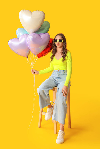 Красива молода жінка з повітряними кульками у формі серця на жовтому фоні - Фото, зображення