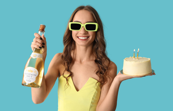 Tatlı pastası ve bir şişe şampanyası olan genç ve güzel bir kadın mavi arka planda doğum gününü kutluyor. - Fotoğraf, Görsel