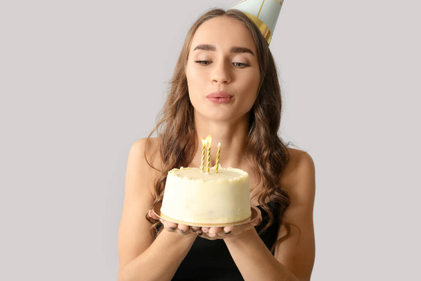 Beautiful young woman in party hat with sweet cake celebrating Birthday on grey background - Photo, Image