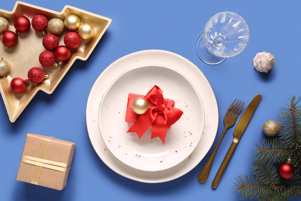 Красивая сервировка стола с рождественскими шарами, еловыми ветвями и подарочной коробкой на синем фоне - Фото, изображение