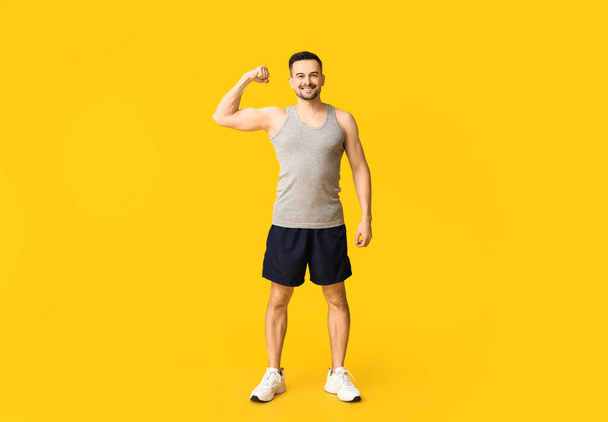 Beau jeune homme sportif montrant des muscles sur fond jaune. Concept de perte de poids - Photo, image