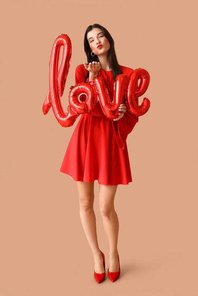 Красива молода жінка з поцілунками на обличчі і повітряних кулях у формі слова "LOVE" на коричневому фоні - Фото, зображення