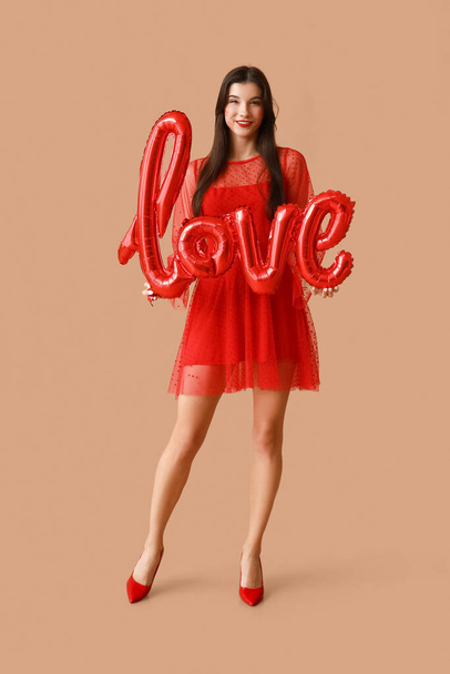 Щаслива молода жінка з поцілунками на обличчі і повітряними кулями у формі слова "LOVE" на коричневому фоні - Фото, зображення