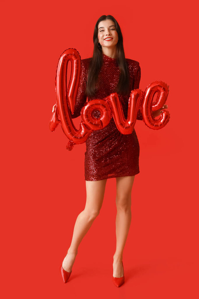 Щаслива молода жінка з поцілунками на обличчі і повітряними кулями у формі слова "LOVE" на червоному тлі - Фото, зображення
