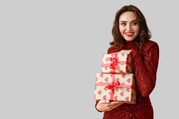 Hermosa joven con cajas de regalo sobre fondo gris - Foto, imagen