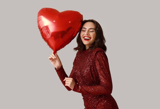 Ευτυχισμένη νεαρή γυναίκα με μπαλόνι αέρα σε σχήμα καρδιάς σε γκρι φόντο - Φωτογραφία, εικόνα