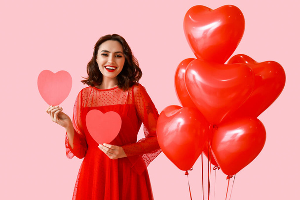 Beautiful young woman with red paper hearts and air balloons on pink background - Photo, Image