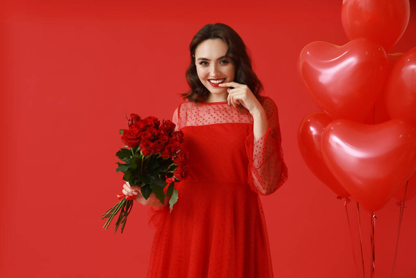 Kırmızı arka planda gül buketi ve kalp şeklinde balonları olan güzel genç bir kadın. - Fotoğraf, Görsel