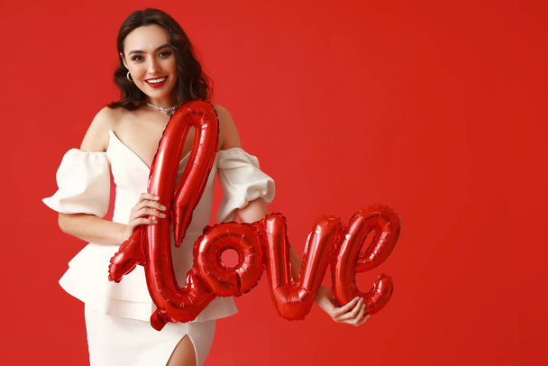 Beautiful young woman with air balloons in shape of word LOVE on red background - Photo, Image