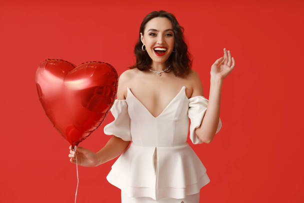 Happy young woman with heart shaped air balloon on red background - Zdjęcie, obraz