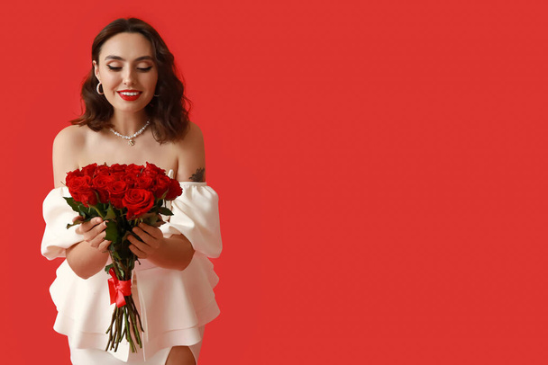 Happy young woman with bouquet of beautiful roses on red background - Photo, Image