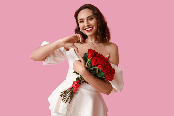 Happy young woman with bouquet of red roses on pink background - Photo, Image