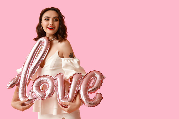 Beautiful young woman with air balloons in shape of word LOVE on pink background - Photo, Image