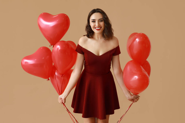 Mooie jonge vrouw met hartvormige luchtballonnen op bruine achtergrond - Foto, afbeelding