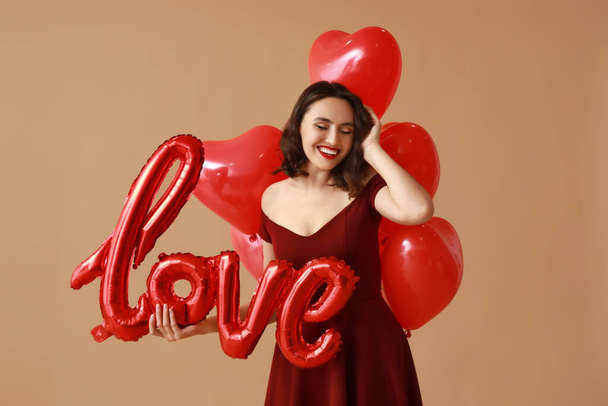 Ευτυχισμένη νεαρή γυναίκα με αερόστατα σε σχήμα λέξης ΑΓΑΠΗ σε καφέ φόντο - Φωτογραφία, εικόνα