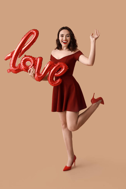 Happy young woman with air balloons in shape of word LOVE on brown background - Photo, Image