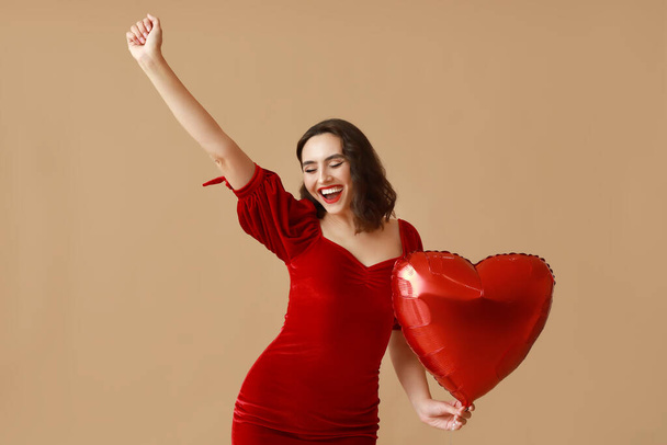 Ευτυχισμένη νεαρή γυναίκα με μπαλόνι αέρα σε σχήμα καρδιάς σε καφέ φόντο - Φωτογραφία, εικόνα