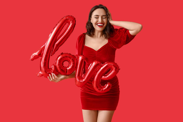 Szczęśliwa młoda kobieta z balonami w kształcie słowa LOVE na czerwonym tle - Zdjęcie, obraz