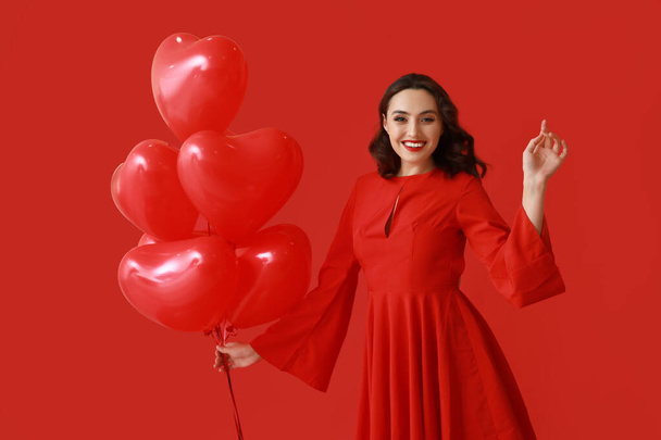 赤い背景に心臓の形をした空気風船を持つ若い女性 - 写真・画像
