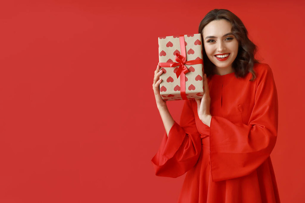 Pretty young woman with gift box on red background - Photo, Image
