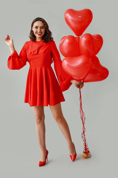 Jovem com balões de ar em forma de coração no fundo cinza - Foto, Imagem