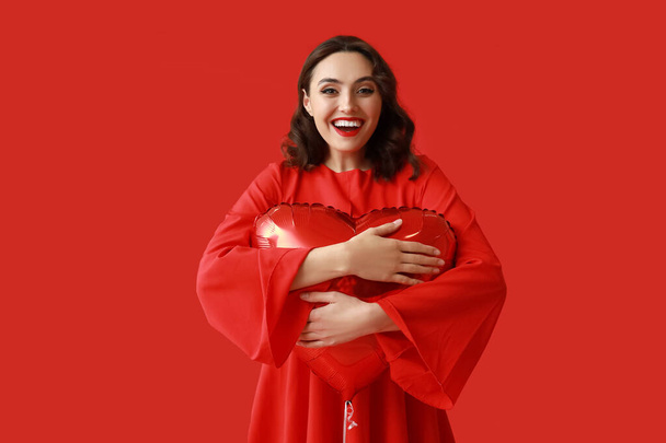 Young woman with heart shaped air balloon on red background - Photo, Image