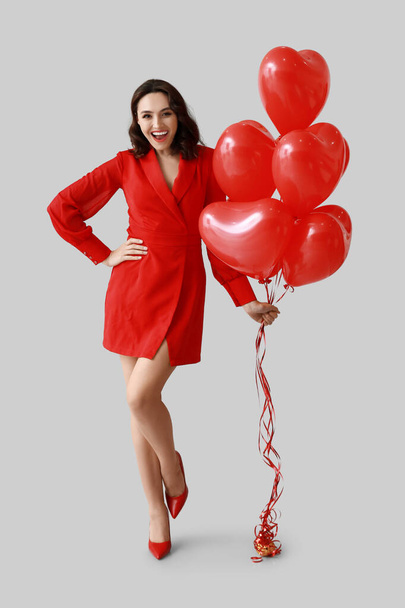 Молодая женщина с воздушными шарами в форме сердца на сером фоне - Фото, изображение