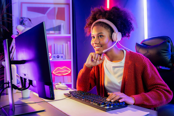 Afroamerykańska dziewczyna serpentyna gra online walki z Esport wykwalifikowany zespół noszenia słuchawek w neonowym kolorze oświetlenie pokoju. Rozmawianie z innymi graczami struganie strategii, aby wygrać konkurentów. Tastemaker. - Zdjęcie, obraz