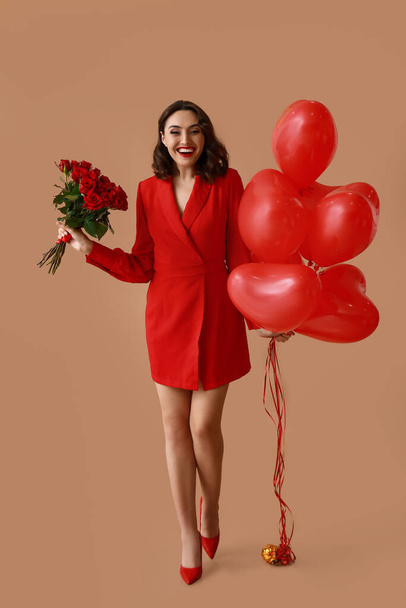 Giovane donna felice con bouquet di rose e palloncini d'aria a forma di cuore su sfondo marrone - Foto, immagini