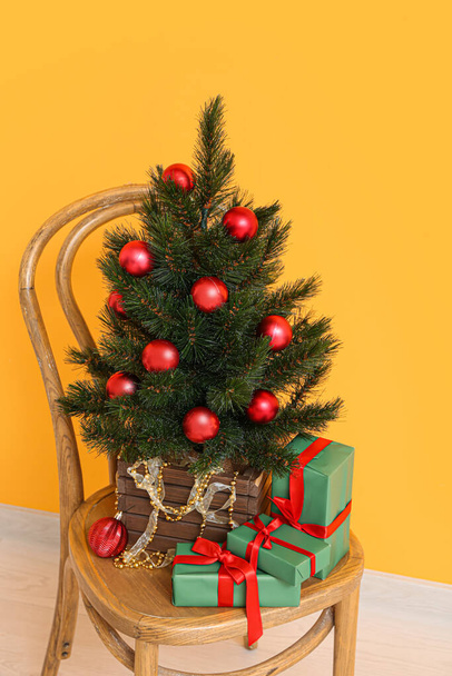 Holzstuhl mit Weihnachtsbaum im Topf und Geschenken in der Nähe der orangefarbenen Wand - Foto, Bild