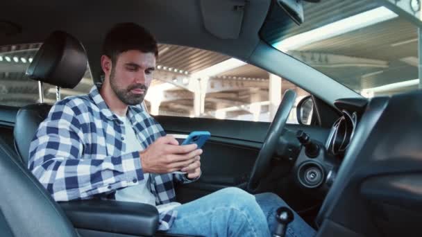 Tipo sentado en el coche mientras sostiene el teléfono inteligente, mecanografía, beber café. Transporte, tecnología, estilo de vida. Movimiento lento - Metraje, vídeo