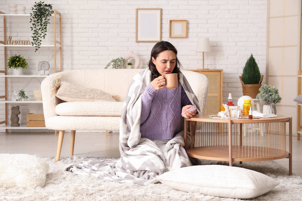 Άρρωστη νεαρή γυναίκα με φλιτζάνι τσάι και χάπια στο σπίτι - Φωτογραφία, εικόνα