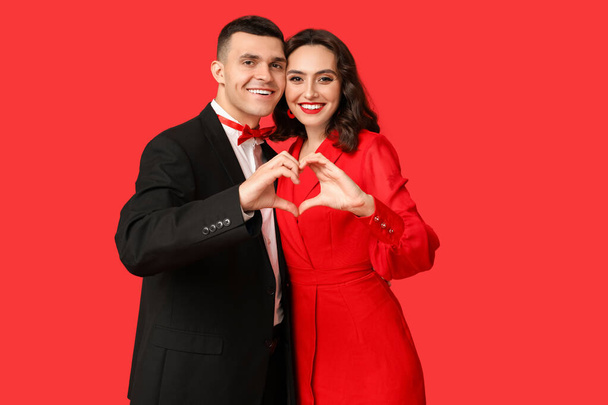 Casal jovem amoroso mostrando gesto cardíaco no fundo vermelho. Celebração do Dia de São Valentim - Foto, Imagem