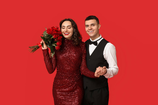 Aimant jeune couple avec bouquet de belles roses sur fond rouge. Célébration de la Saint Valentin - Photo, image