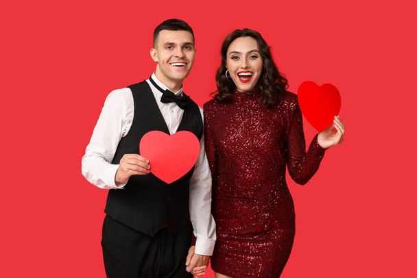 Amante pareja joven con corazones de papel sobre fondo rojo. Celebración del Día de San Valentín - Foto, imagen