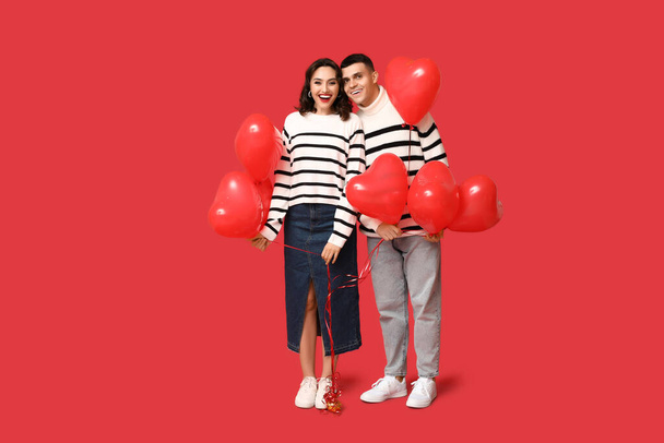 Amante pareja joven con globos en forma de corazón sobre fondo rojo. Celebración del Día de San Valentín - Foto, Imagen