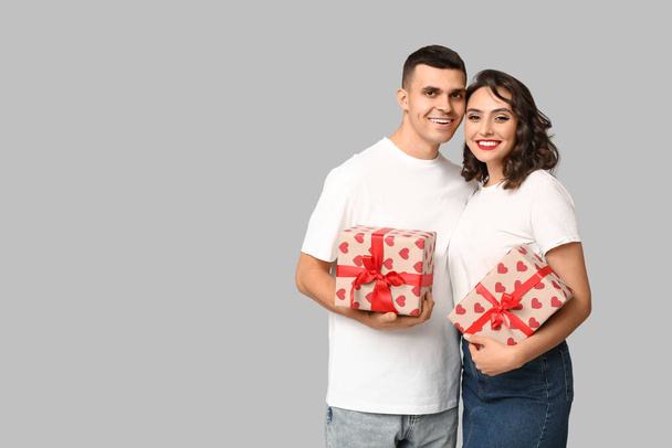 Amare giovane coppia con scatole regalo su sfondo grigio. Celebrazione del giorno di San Valentino - Foto, immagini