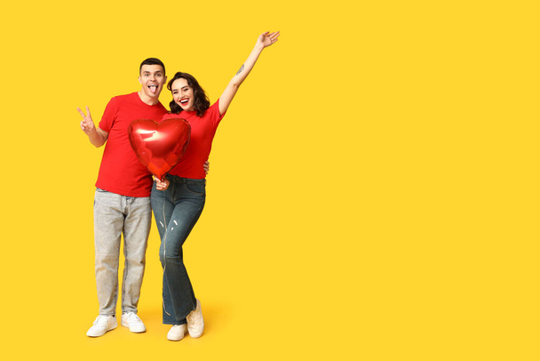 Любляча молода пара з повітряною кулею у формі серця, що показує жест перемоги на жовтому тлі. Святкування Дня святого Валентина - Фото, зображення